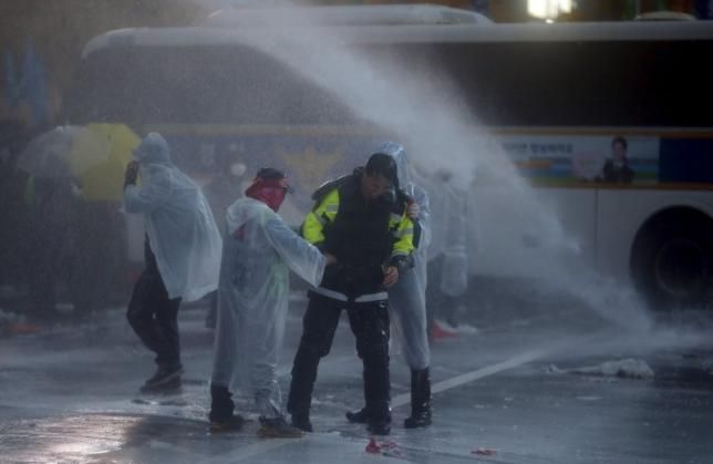 Một cảnh sát chống bạo động Hàn Quốc bị người biểu tình giữ lại đứng cùng khi họ bị phuôn vòi rồng và hơi cay để giải tán. Ảnh: Reuters. 